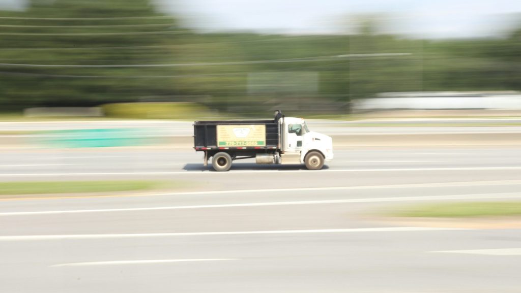 a white truck driving down a street next to a forest